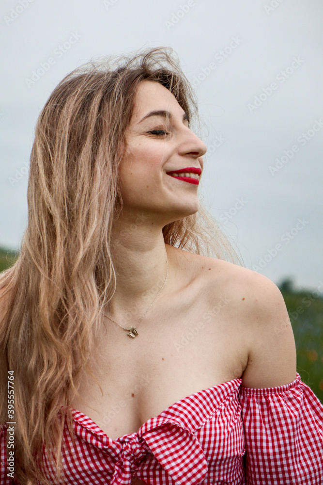 The girl is sincerely smiling. Blond and wavy hair. Stylish red clothes for women. Lips painted with red lipstick. The girl is sincerely smiling. Blond and wavy hair. Stylish red clothes for women. Lips painted with red lipstick.
