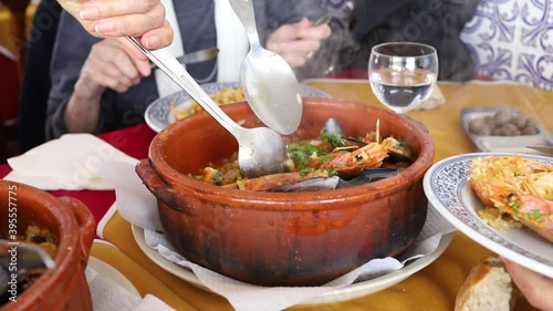 people eating typical portuguese dish rice with seafood in red ceramic pot in restaurant