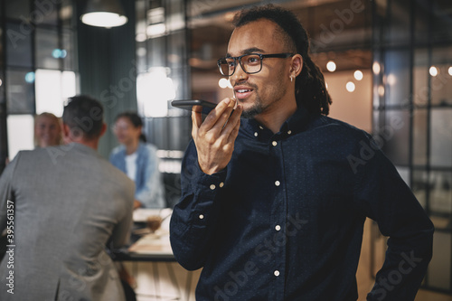 Photos Young businessman talking on speakerphone while working in an of