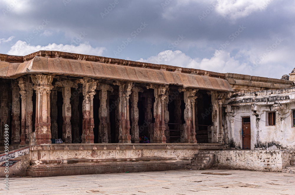 Hampi, Karnataka, India - November 4, 2013: Virupaksha Temple complex. Ruined open pillared hall in beige and dark brown stone under blue cloudscape.
