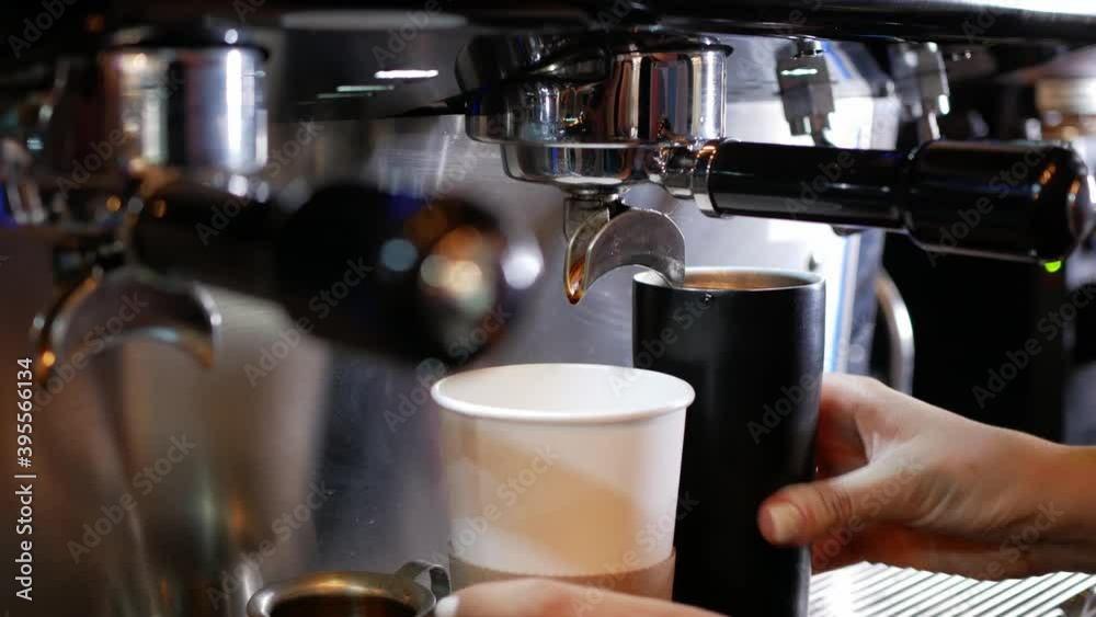 A girl inserts a coffee holder into the coffee machine and pours the coffee into cups of client