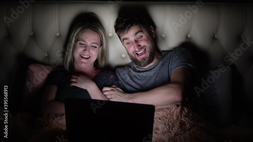 Man and woman, young couple watching funny movie on laptop in bed before going to bed