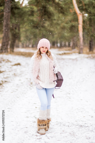 beautiful young woman in light clothes with a backpack walks in a winter snow-covered forest.