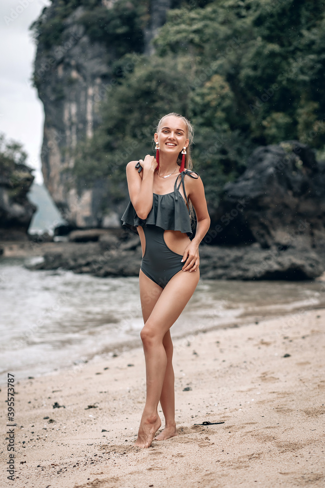 Obraz premium Girl Blonde in a gray fashion swimsuit on the beach with white sand near the ocean on vacation. A beautiful model with a sexy body is sunbathing on the sand on the beach in Thailand in Phuket.
