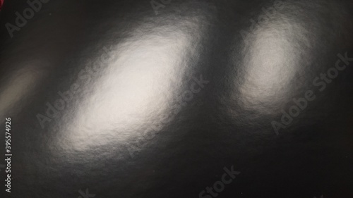 Glare of light on shiny gray paper. Several light spots on a dark surface that reflects light. Abstract monochrome background.