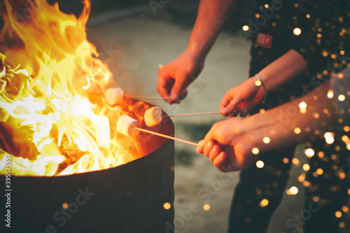 Human hands holding sticks for open fire marshmallow roasting at night time. Close view background with place for text