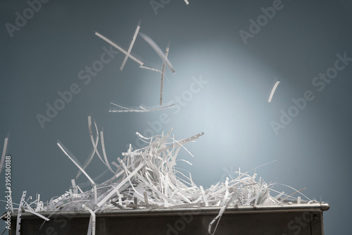A pile of shredded paper strips lie in a metal box and from above  more strips fall down with motion blur.