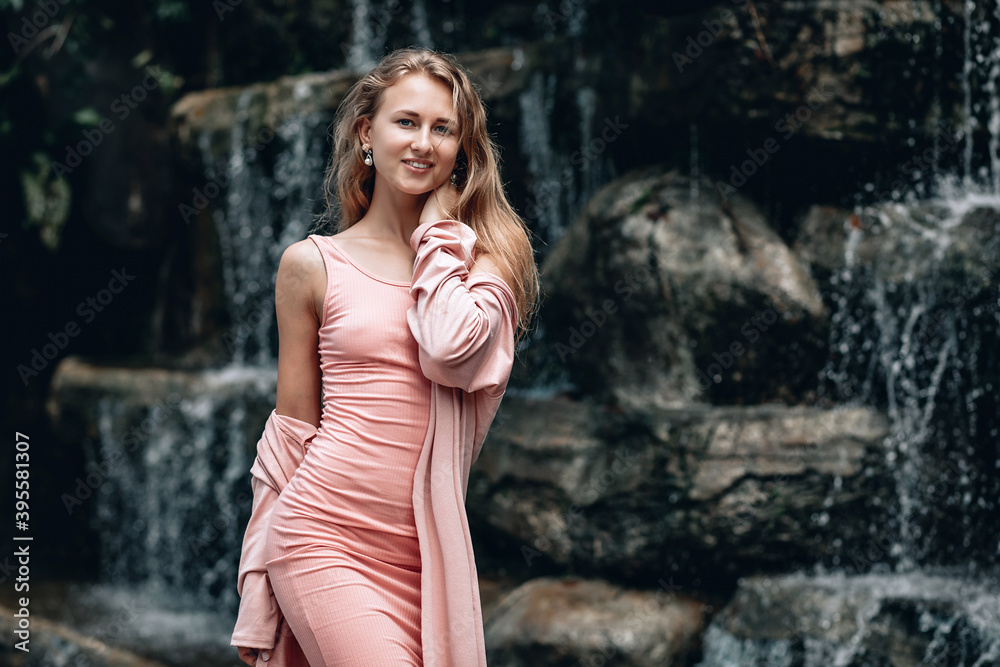 Obraz premium Young woman in pink dress posing near blurred waterfall. Kuala Lumpur. Malaysia.