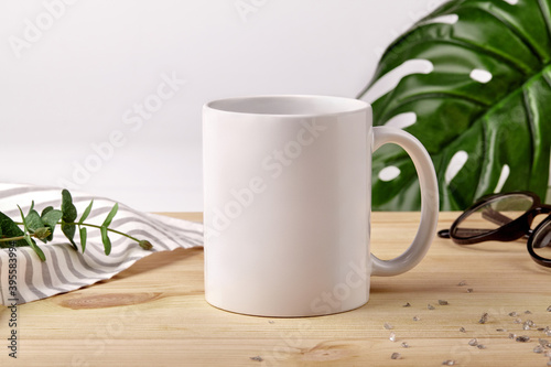 Ceramic mug on wooden desktop next to striped tablecloth  scattered crystals and green plants on white background. Close up  copy space