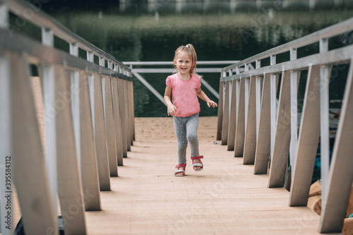 Smiling little caucasian kid girl in pink t-shirt and blue jeans running up metal stair. - Image.