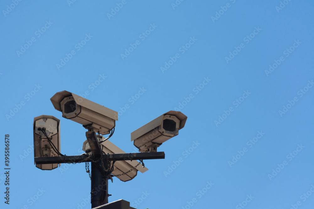 Four security cameras on a pole in the street, from below, with a blue sky. Concepts like security or privacy