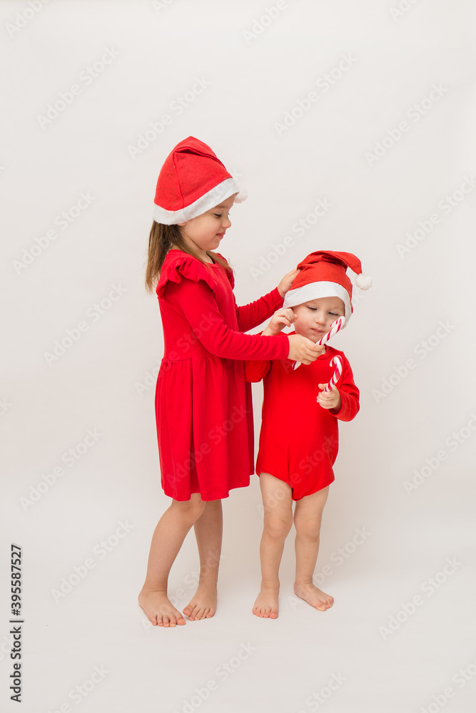 Obraz premium a little girl and a full-length boy in red caps with lollipops on a white background with a copy of space