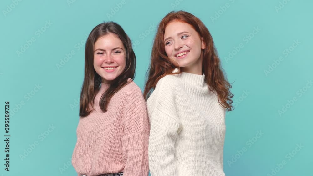 Side profile view two smiling young brunette redhead women friends 20s in casual pastel pink white sweaters standing back to back isolated on blue background studio portrait. People lifestyle concept Side profile view two smiling young brunette redhead women friends 20s in casual pastel pink white sweaters standing back to back isolated on blue background studio portrait. People lifestyle concept