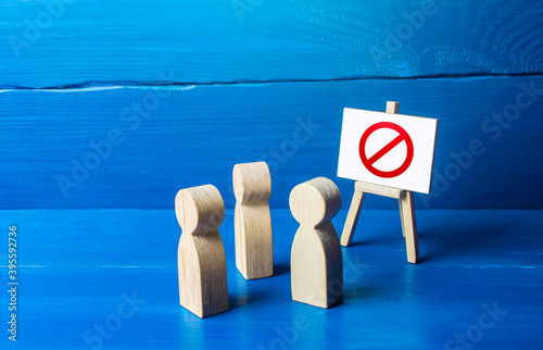 Φωτογραφία A group of people figurines looking at an easel with a red prohibitory symbol NO