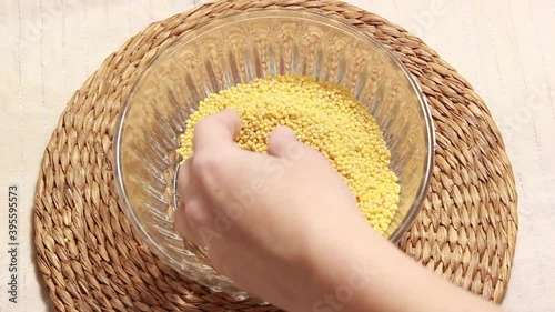 Raw millet falls from a woman's hand into a glass plate. Close-up, selective shot. photo