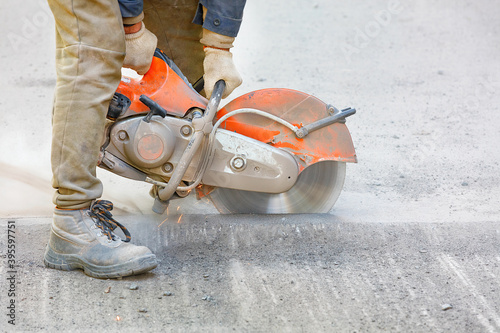 The builder cuts the old asphalt with a portable petrol cutter and a diamond cutting disc, creating a cloud of dust and sparks. photo