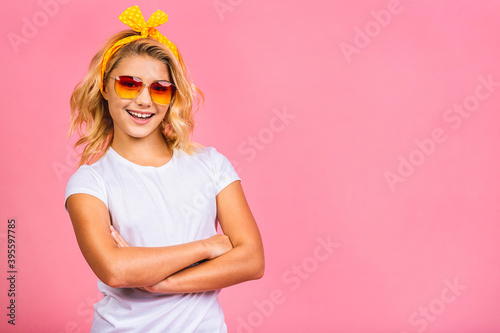 Cool little blonde girl. Charming teenage kid girl in fancy sunglasses grinning and posing for the camera isolated over pink background.