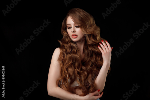 Beauty portrait of elegant young woman. Glamour makeup. Face of the beautiful woman with long brown curly hair posing at studio over dark background. Sensual portrait. © Maxim