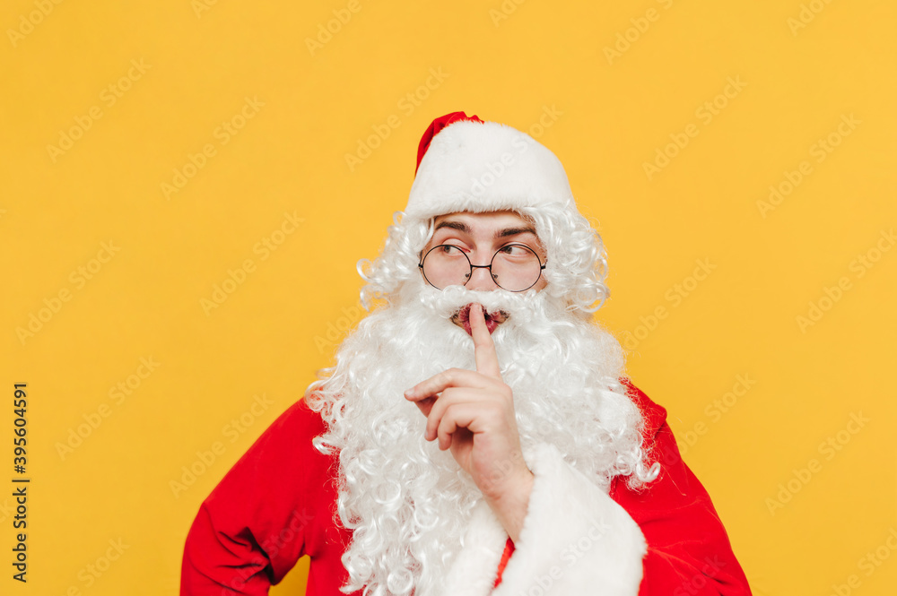 Man in a Santa Claus costume is expressing a silent gesture, hiding a secret. Santa is showing a hush gesture by touching his lips with his finger.