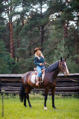 Smilng pretty young cowgirl. A cowboy style female in a plaid shirt sitting on a horse and holding a cowboy hat.