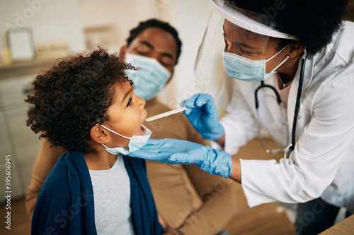 Obraz na plátne African American doctor with face mask examining boy's throat during a home visit