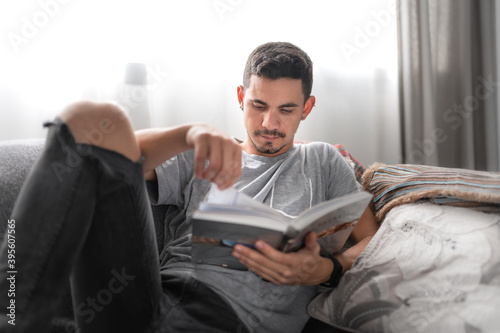 Fototapeta Naklejka Na Ścianę i Meble -  young man lying on a sofa, reads a book