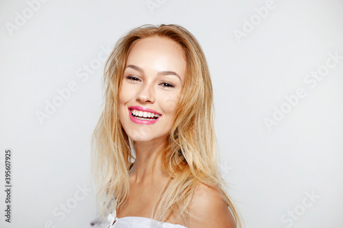 Happy blonde young woman with beautiful natural makeup and long wavy hair, with bare shoulders, over white background.