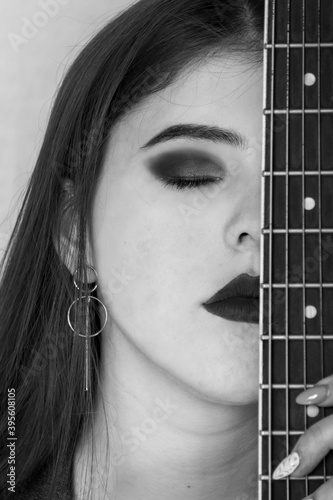 Portrait of a girl in black and white style with long hair. A piece of guitar near the face of a young woman.
