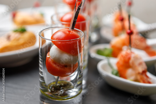 Cherry tomatoes and mozzarella canapes on skewers in a glass glass with a background of king prawns in close-up