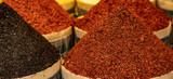 Photo of condiments that are sold at the market in Istanbul. In the foreground, red ground chili pepper and ground black pepper