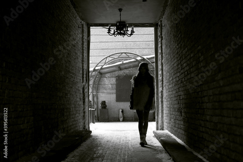 Young brunette girl  wearing grey fur coat and knit hat  walking in passageway of old historical building. Winter female portrait outside.Tourist on sightseeing tour in snowy city town.