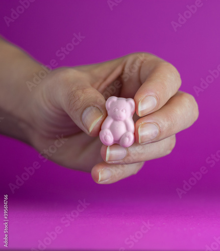 Pink gummy bear held by a woman. Colorful, pink background.