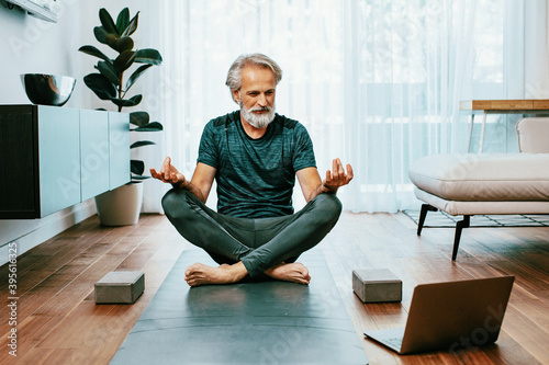 Portrait of a senior white hair man in yoga pose watching lesson from laptop computer