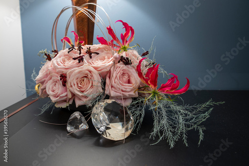 lovely floral arrangement with avalanche roses, gloriose and fake dimonds on a table with copper lamp and dark blue wall in the background