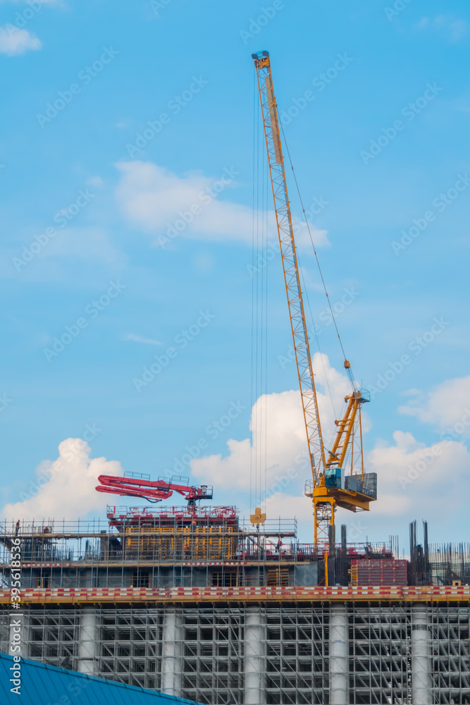 Moving yellow tower cranes and unfinished building construction against summer cloudy blue sky. Building process, architecture, urban, engineering, city developing industrial concept