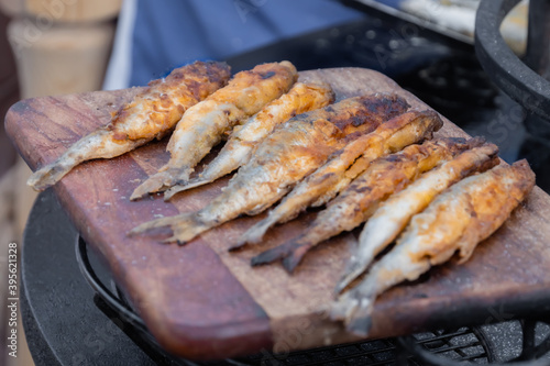 Crispy breaded european smelt fish on wooden cutting board at summer outdoor food market: close up. Seafood, barbecue, gastronomy, cookery, street food concept