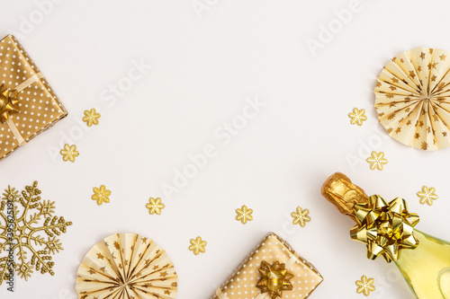 Festive white background with gold decoration , bottle of sparkling wine and gift box, paper christmas tree decorations and glittering snowflakes , flat lay, top view, copy space