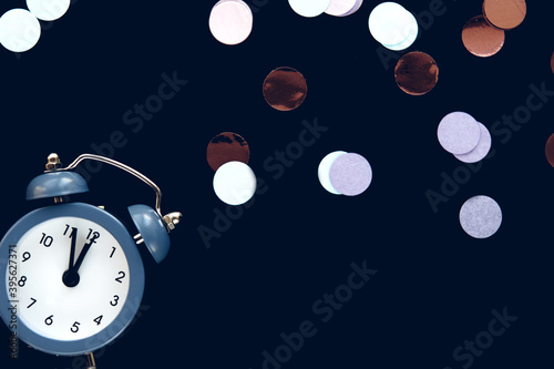 Blue vintage alarm clock shows 12 o'clock isolated on dark background with sparkling round confetti metafan. Wake up and hurry up. Countdown to midnight new year photo