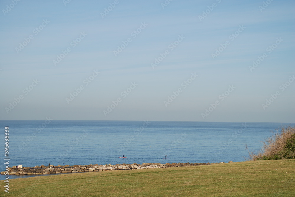Blue sea water under a light sky.
Winter sunny day on the mediterranean sea. The smooth surface of the water stretches to the horizon. A strip of green shore with a breakwater and bushes. ...