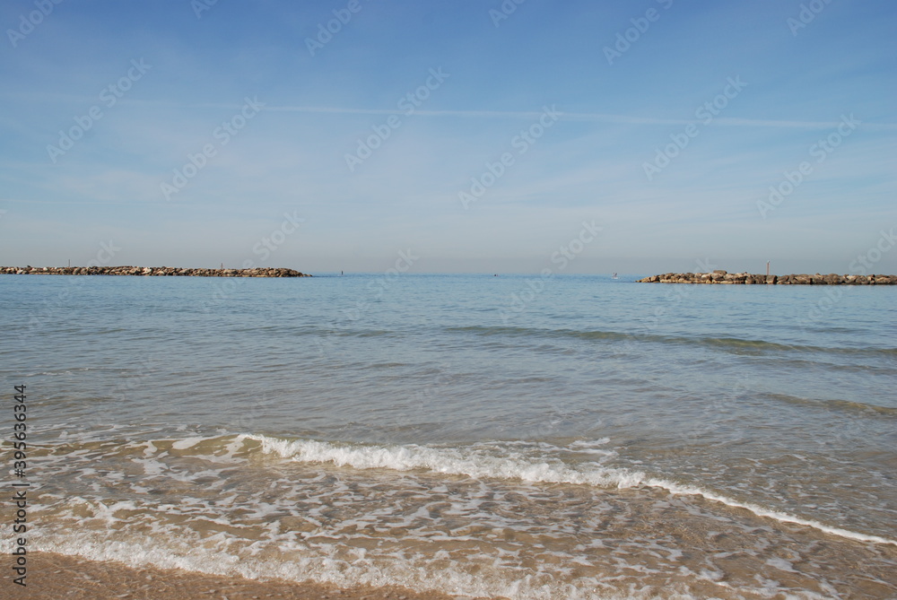 Two breakwaters protect the beach from the waves.
Winter sunny day on the mediterranean sea. Sea water stretches to the horizon. Small waves are splashing along the coast.