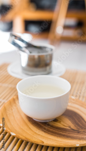 Beautiful porcelain tea cup on a saucer. Huang Shan Mao Feng green tea from Anhui province, China. Very hydrating and energising beverage. Spring harvest. Vertical close up shot.