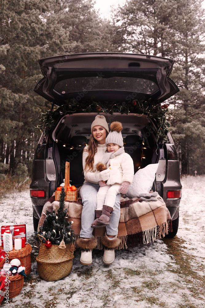 preparation for Christmas. Mom and little daughter have fun playing in the trunk of a car. Cold winter, snowy weather.