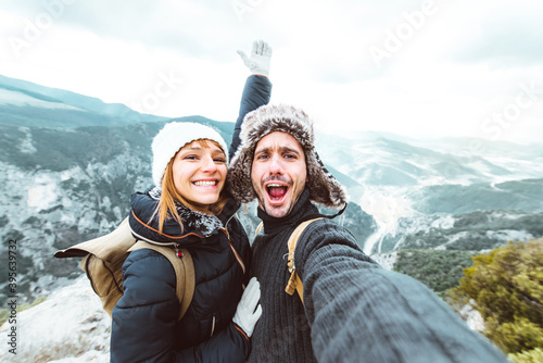 Happy couple taking a selfie hiking mountains - Successful hikers on the top of the peak smiling at camera 