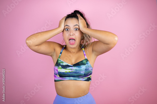 Young beautiful woman wearing sportswear over isolated pink background crazy and scared with hands on head, afraid and surprised of shock © Irene