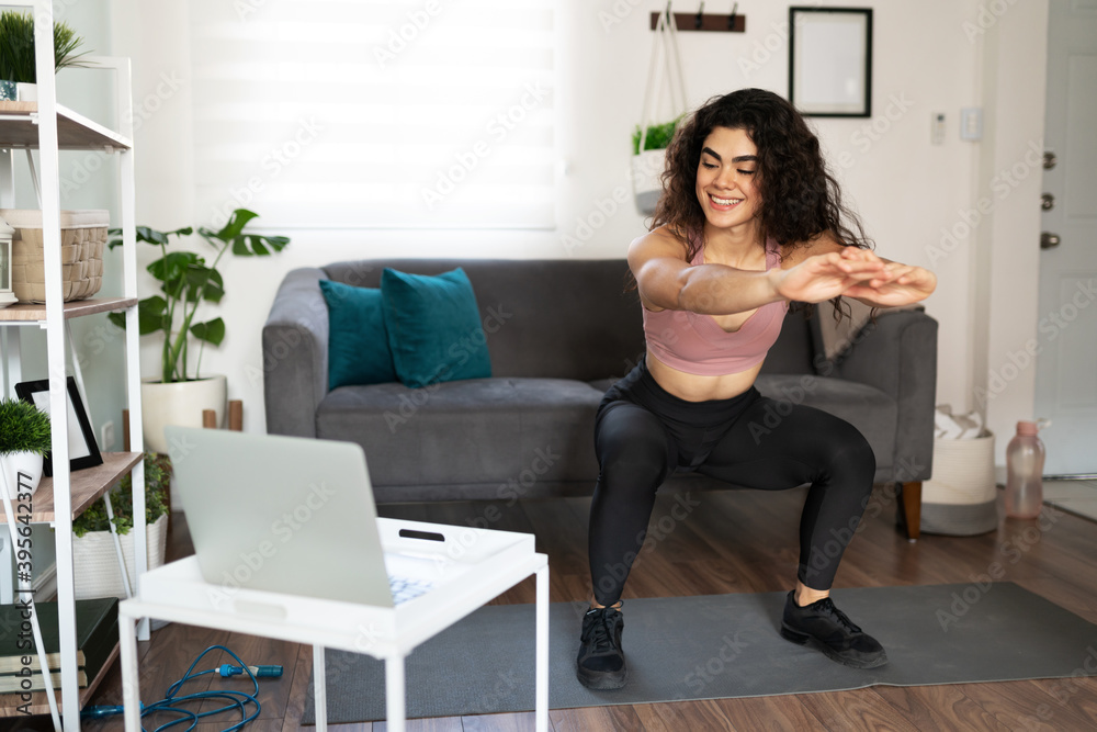 Young woman smiling while doing squats with an exercises video Young woman smiling while doing squats with an exercises video