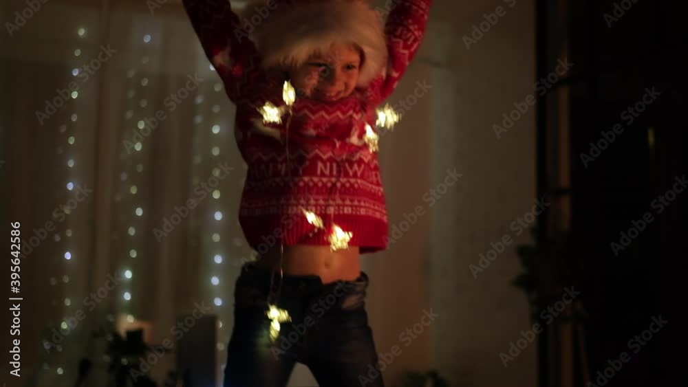 Excited Christmas boy jumping dancing in Santa hat at home evening. New Year and Holidays. Christmas happiness. Child having fun.