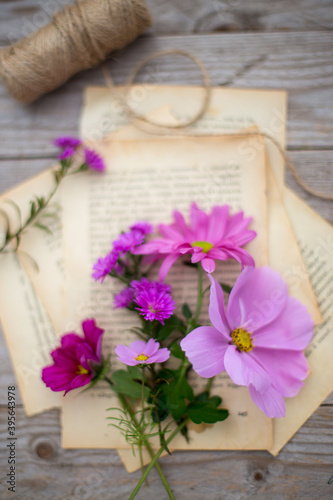 Mazzetto di fiori autunnali nella tonalità del rosa appoggiati su una serie di fogli su un tavolo 