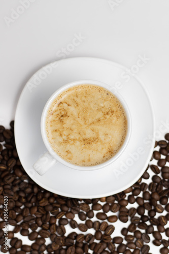 White clean background from above with a cup and saucer filled with coffee and half sprinkled with coffee beans.