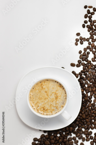 White clean background from above with a cup and saucer filled with coffee and coffee beans scattered in the corner.