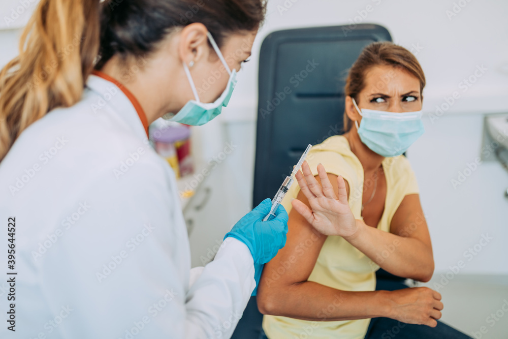 Female doctor or nurse trying to give shot or vaccine against virus to a scared patient. Angry and distrustful patient refuses to receive it.